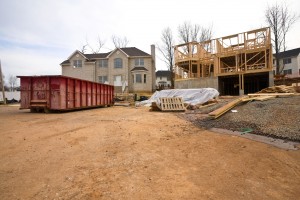 Two houses, one framed and one finished sit unoccupied with a large red dumpster
