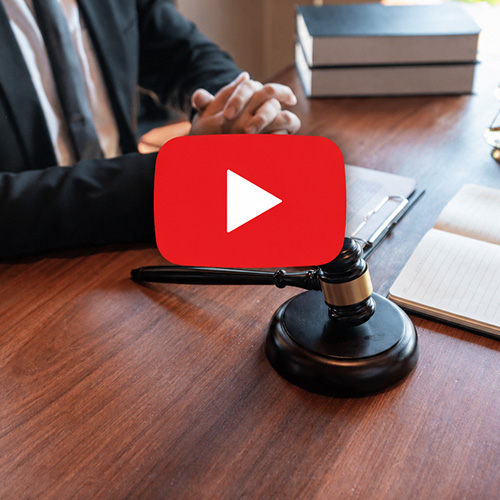 Attorney at desk with gavel, law books, and notebook, YouTube play icon for legal advice video
